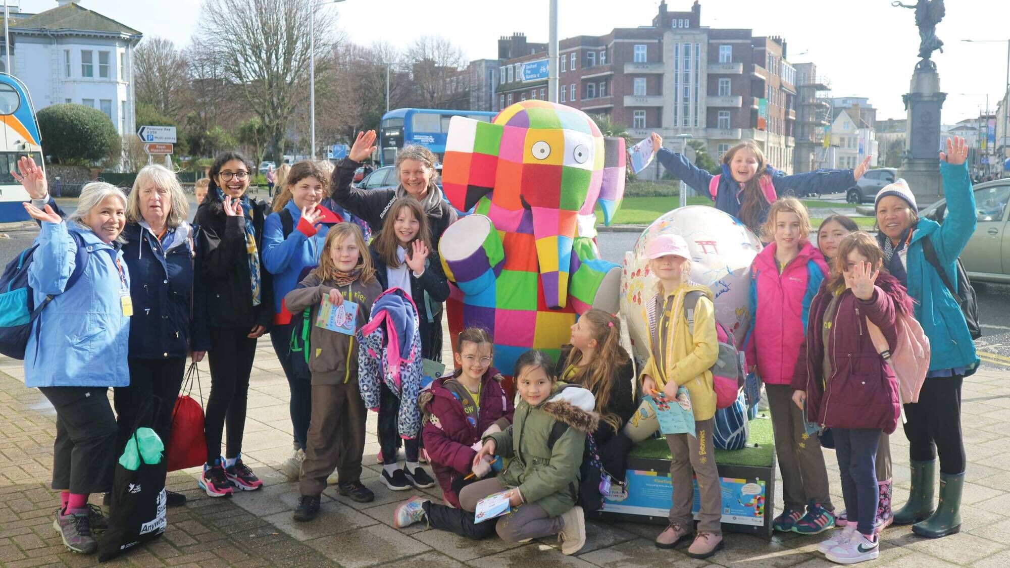 A group of young girls and their leaders waving beside a colourful patchwork elephant sculpture in Eastbourne