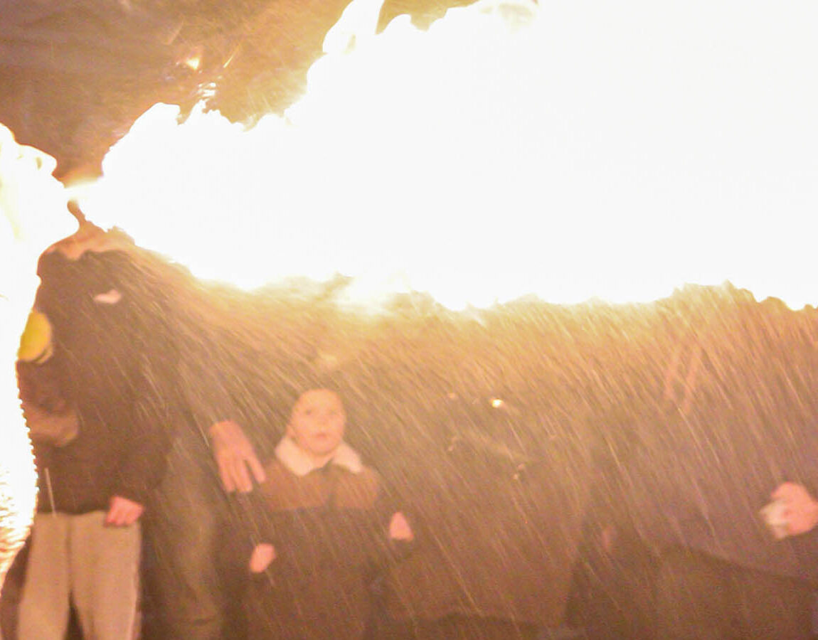 A burst of flame from a fire performer lights up a crowd of families at night