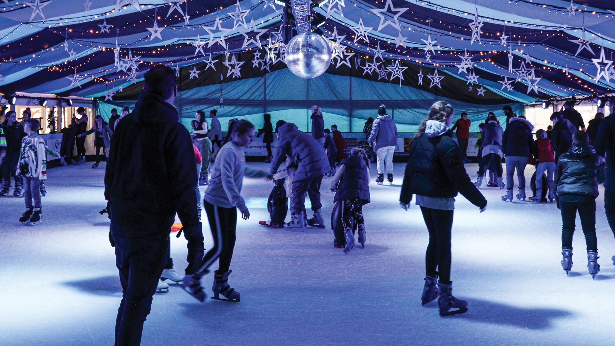 Families skating on an ice rink under a canopy of stars and fairy lights